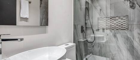 A modern bathroom with a white sink, a glass-enclosed shower, and a marble backsplash.