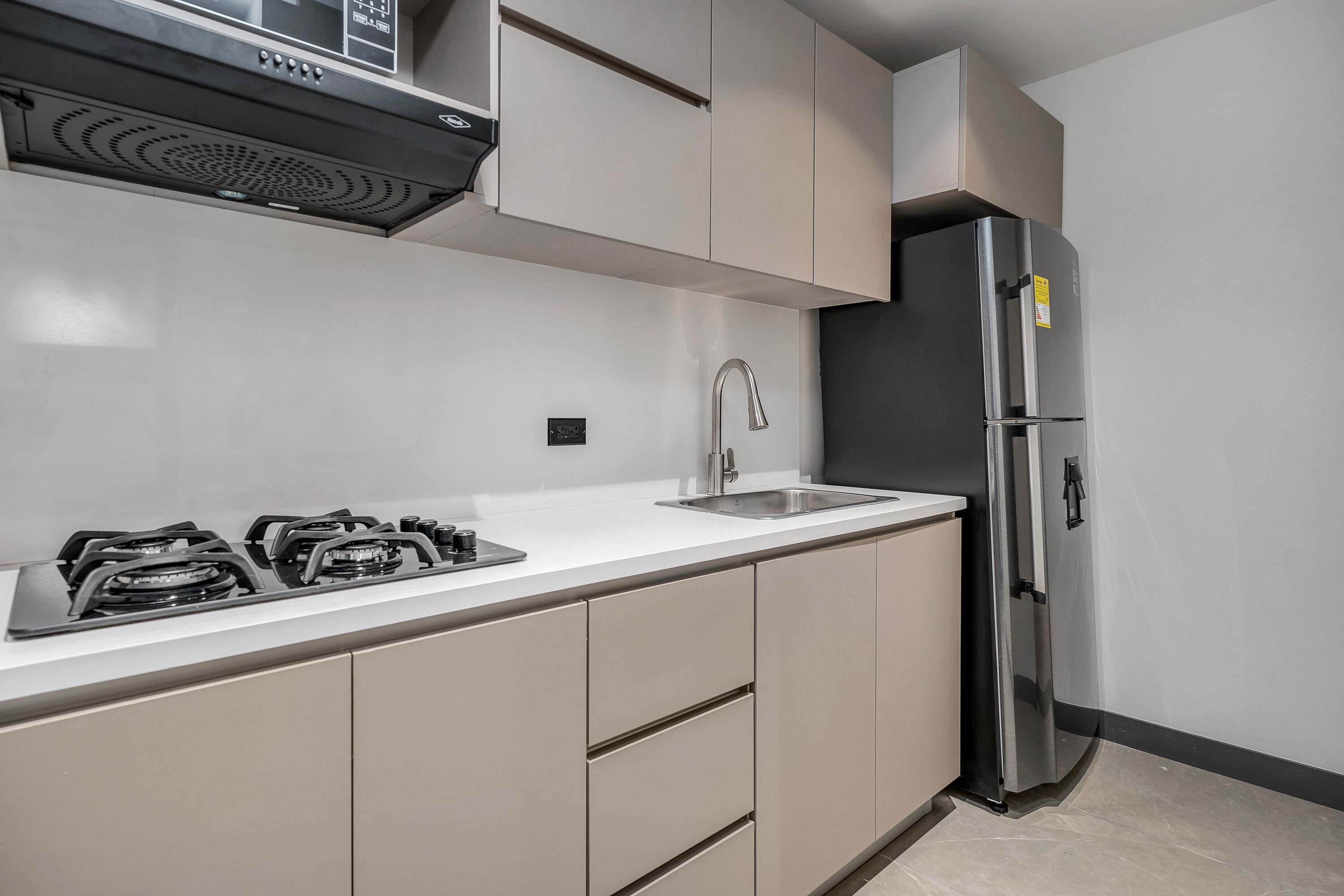 A modern kitchen with a gas stove, stainless steel refrigerator, and beige cabinetry.