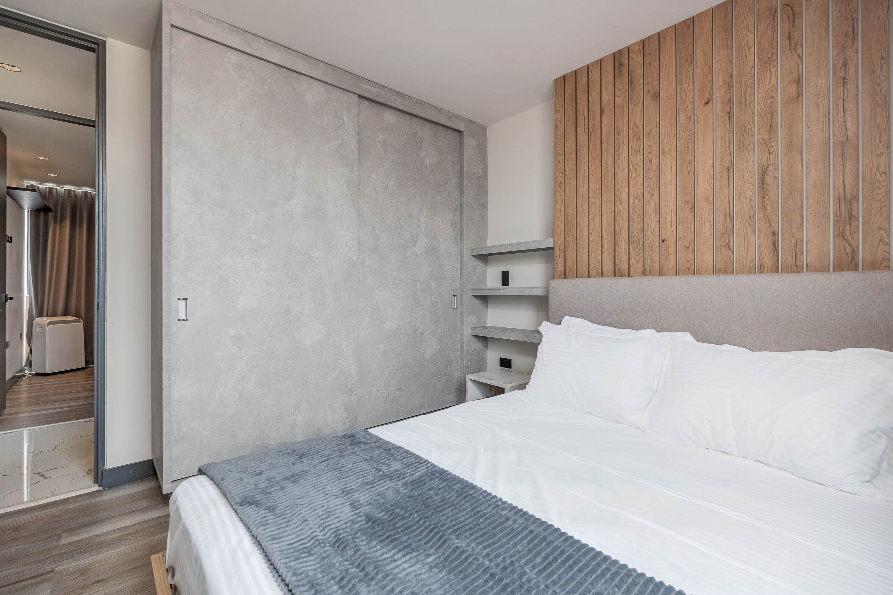 Une chambre à coucher moderne avec un grand lit, une armoire grise et un lambris en bois sur le mur.