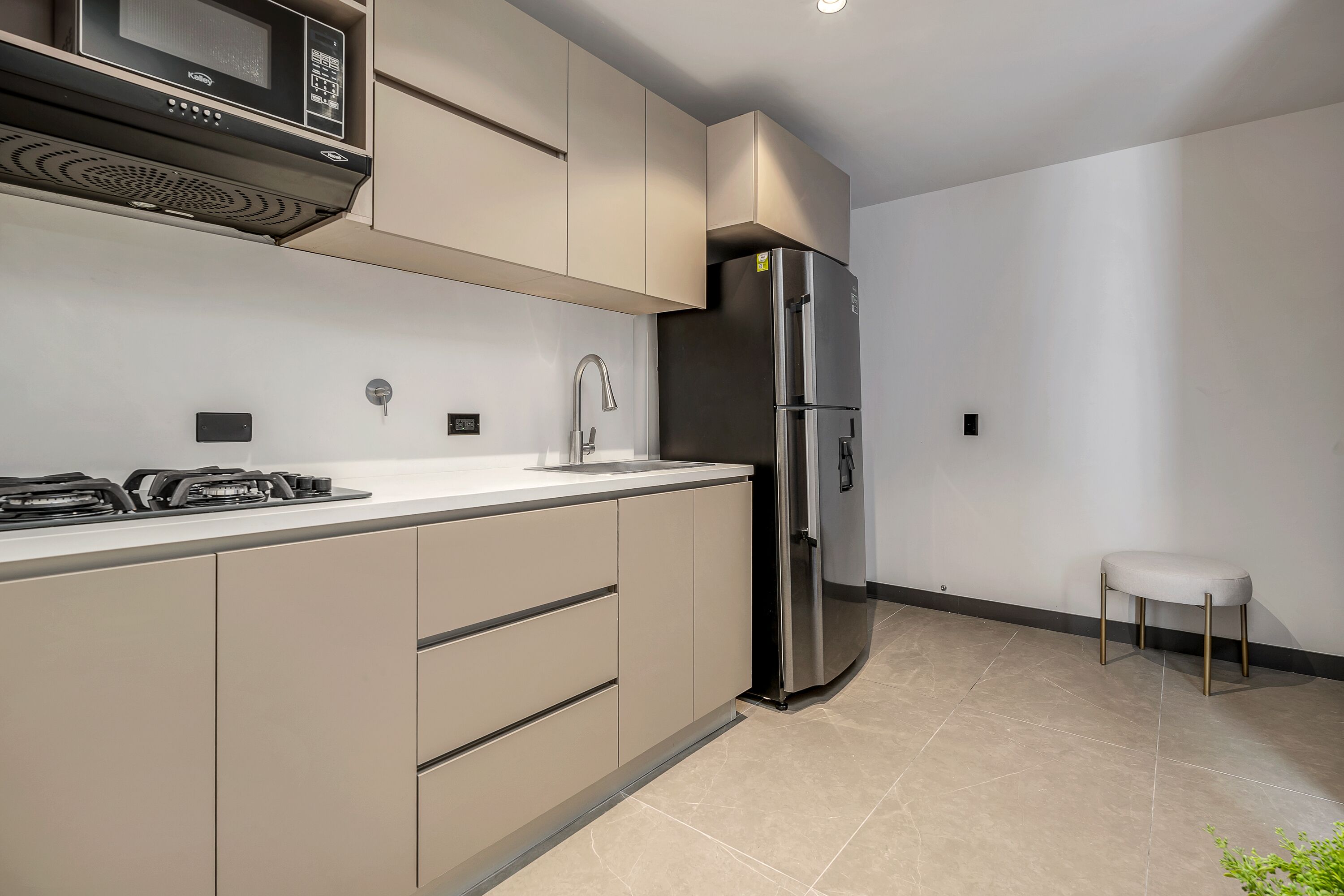 Une cuisine moderne avec des meubles de couleur beige, un réfrigérateur en acier inoxydable, un four à micro-ondes et une cuisinière à gaz.