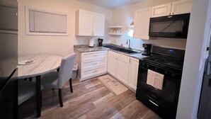 A compact kitchen with white cabinets, a black stove, a microwave, and a dining area with a table and chairs.
