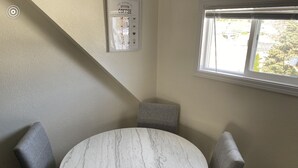 A round marble table with four grey upholstered chairs in a corner of a room with a window.