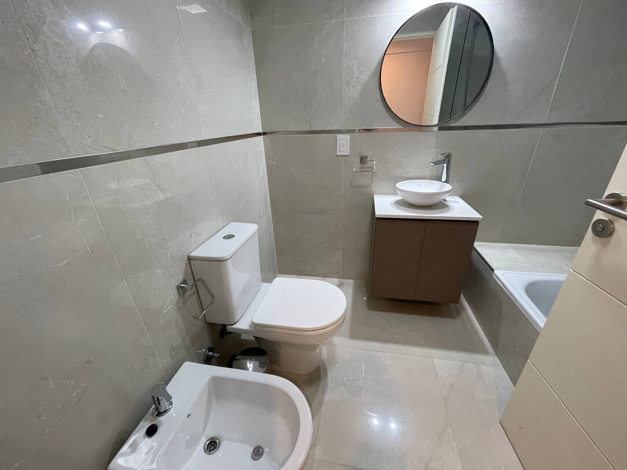 A modern bathroom with a toilet, bidet, sink, and a mirror.
