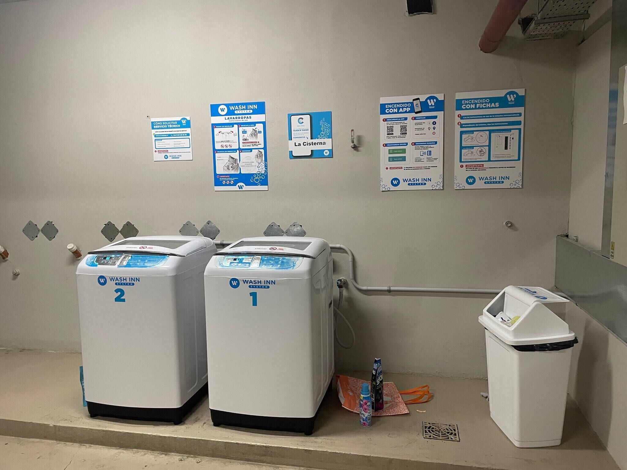 A restroom with two Wash Inn sinks, a trash bin, and informational posters on the wall.