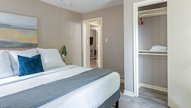 Un dormitorio con una cama, ventilador de techo, un cuadro y vestidor.