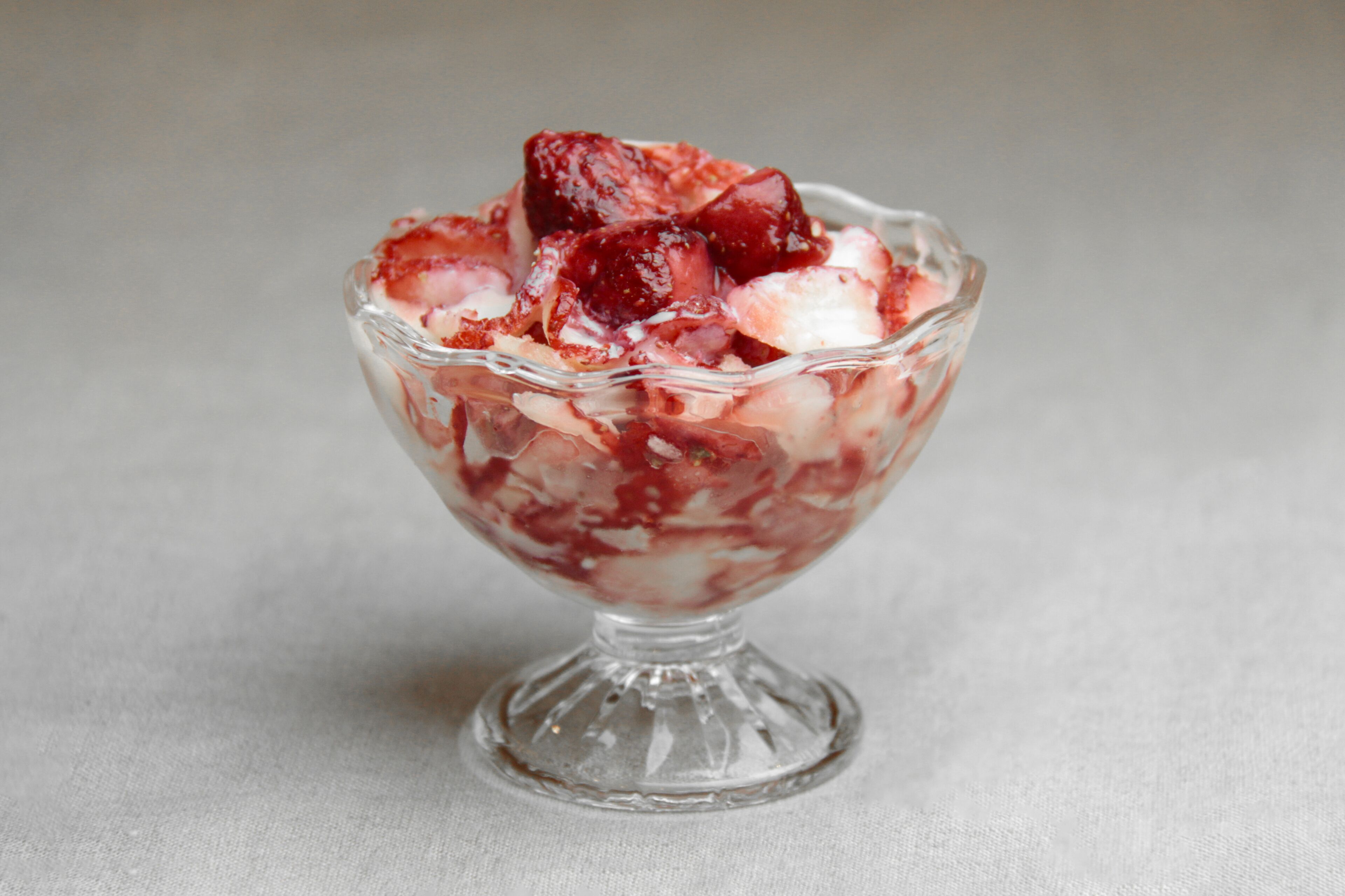 A clear glass bowl containing a dessert with visible fruit pieces and a creamy base.