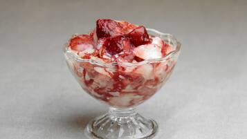 A clear glass bowl containing a dessert with visible fruit pieces and a creamy base.