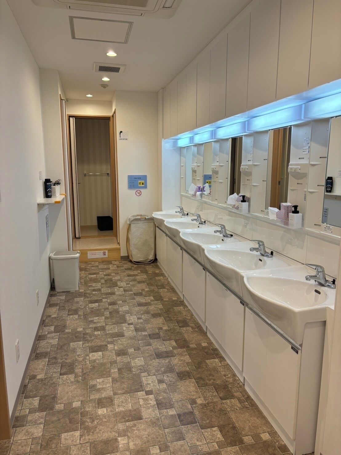 A hotel bathroom with multiple sinks, a large mirror, and a trash bin.
