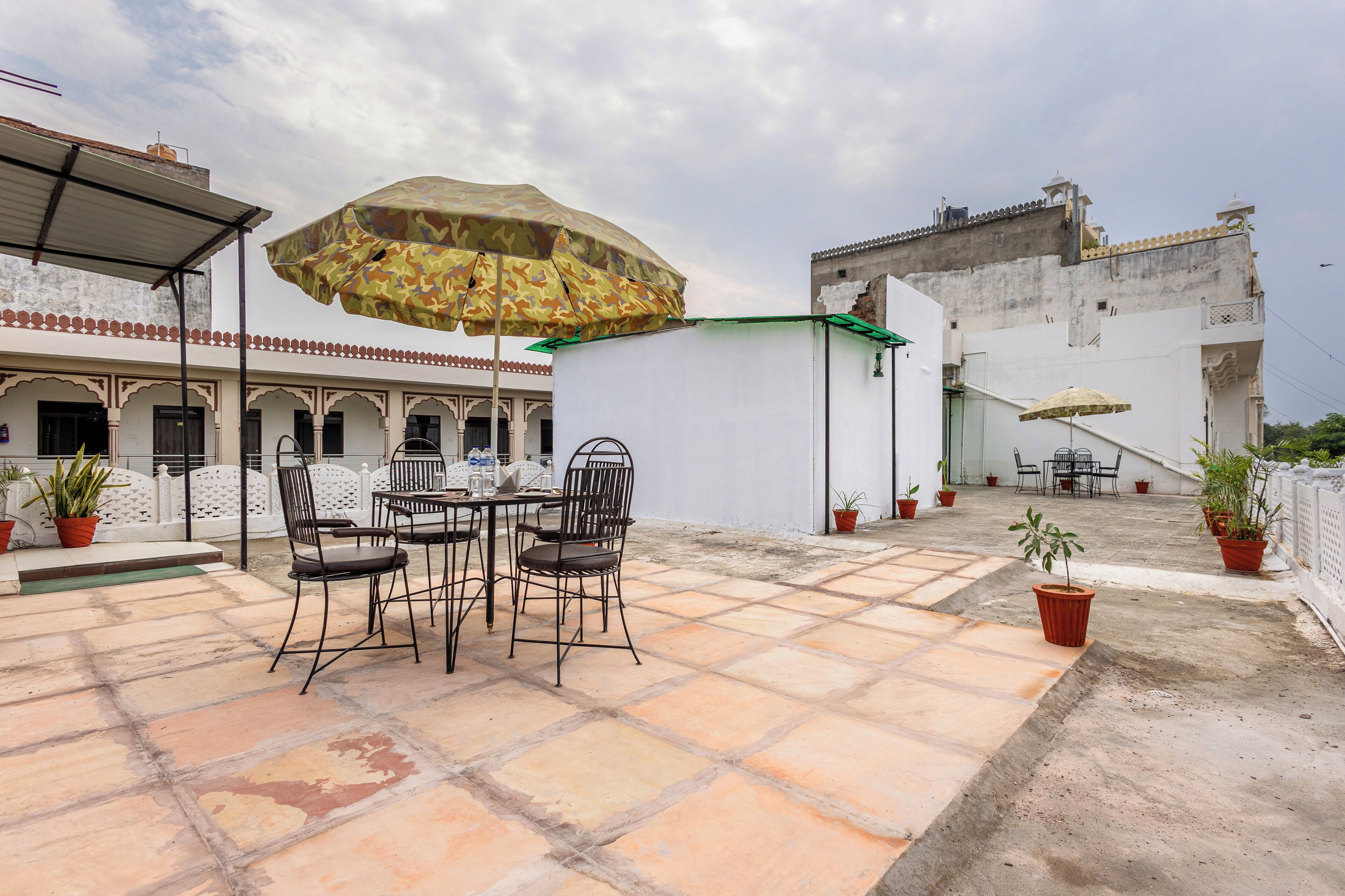 Una terraza en la azotea con una mesa, sillas, plantas en macetas y un paraguas grande.