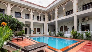 Piscina com espreguiçadeiras, rodeada por vasos de plantas e arcos arquitetônicos.
