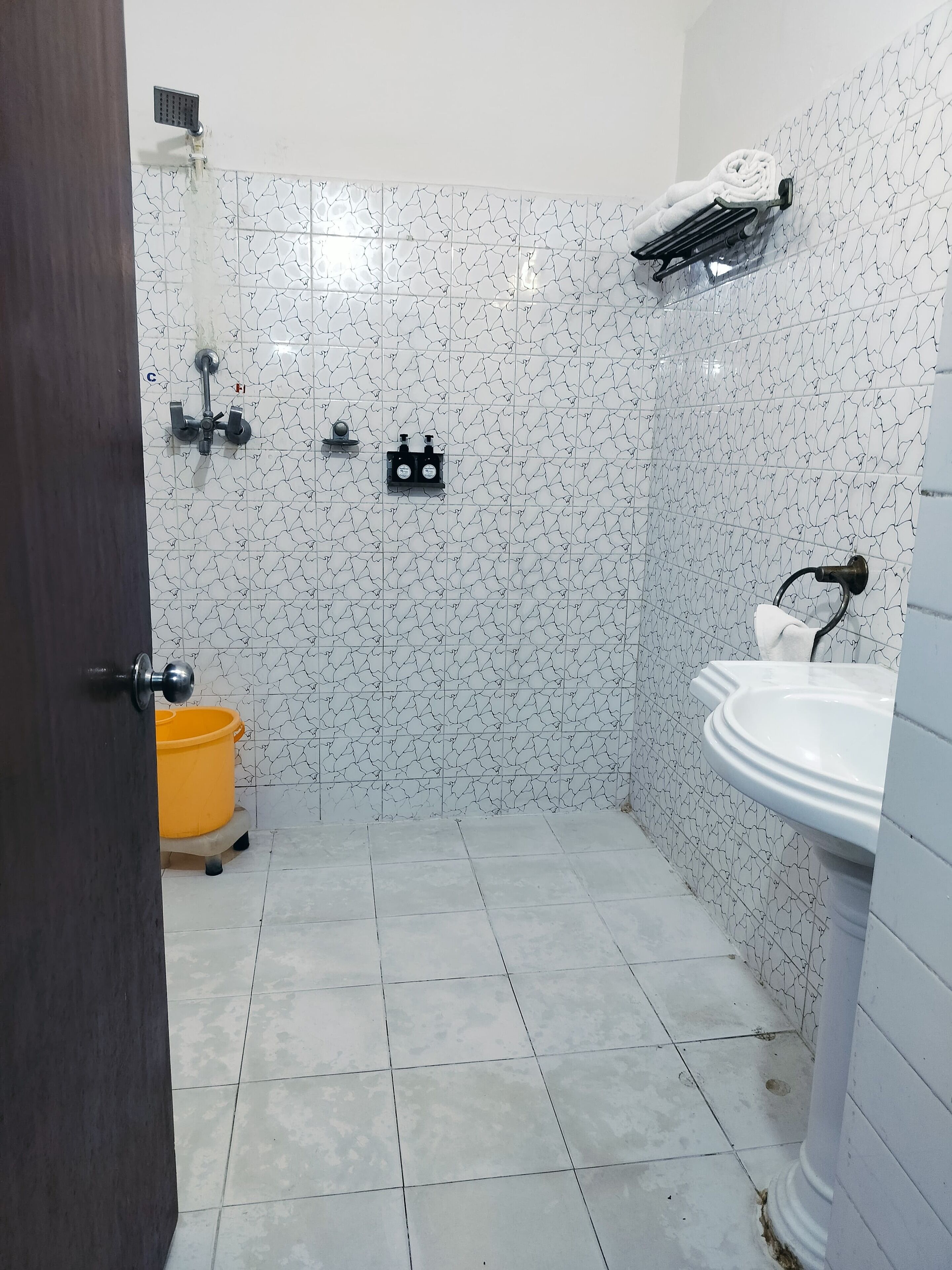 A bathroom with white tiled walls, a yellow bucket, a sink, and a shower.