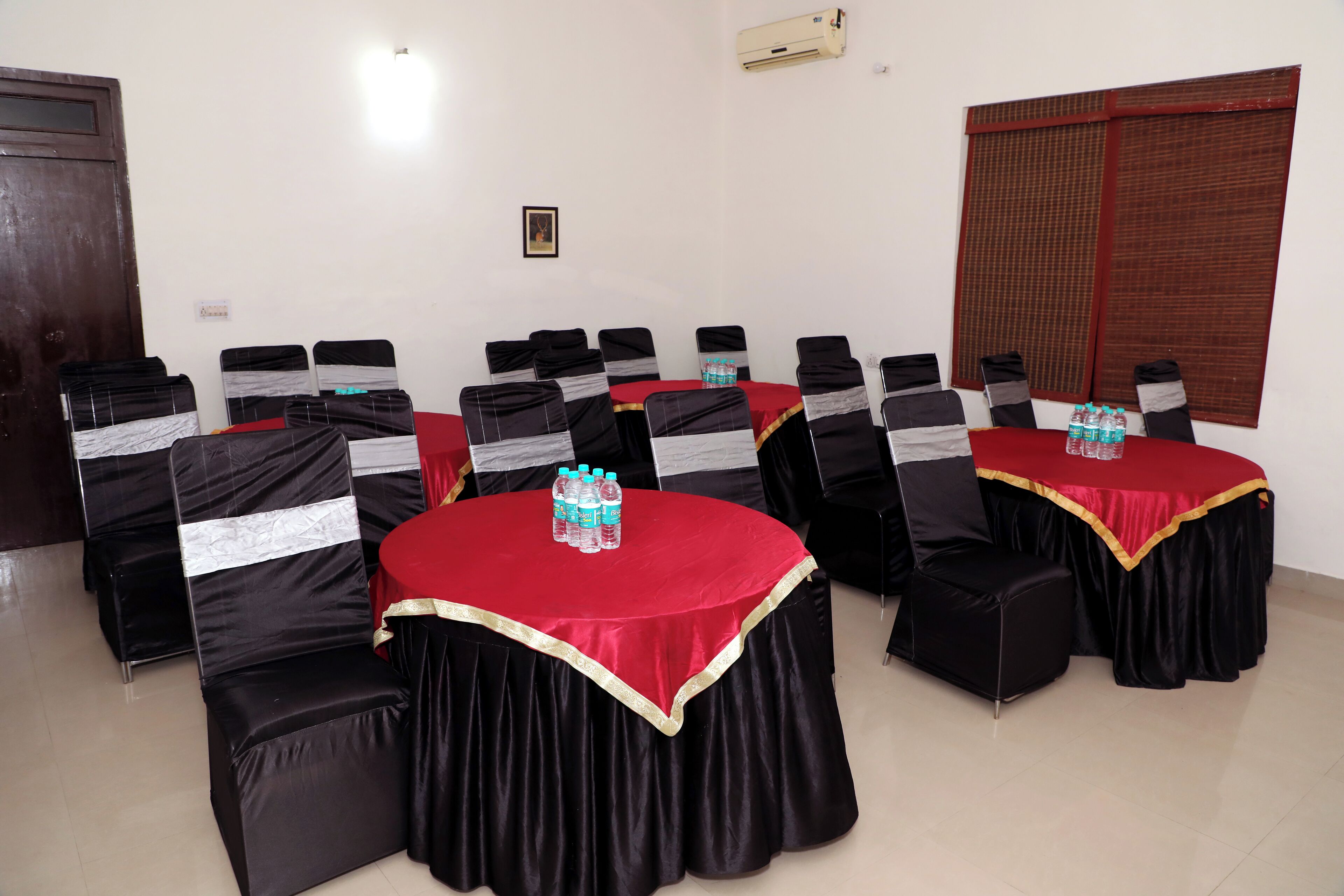 Une salle de conférence avec des tables rondes, des chaises noires ornées de rubans blancs et des nappes rouges.