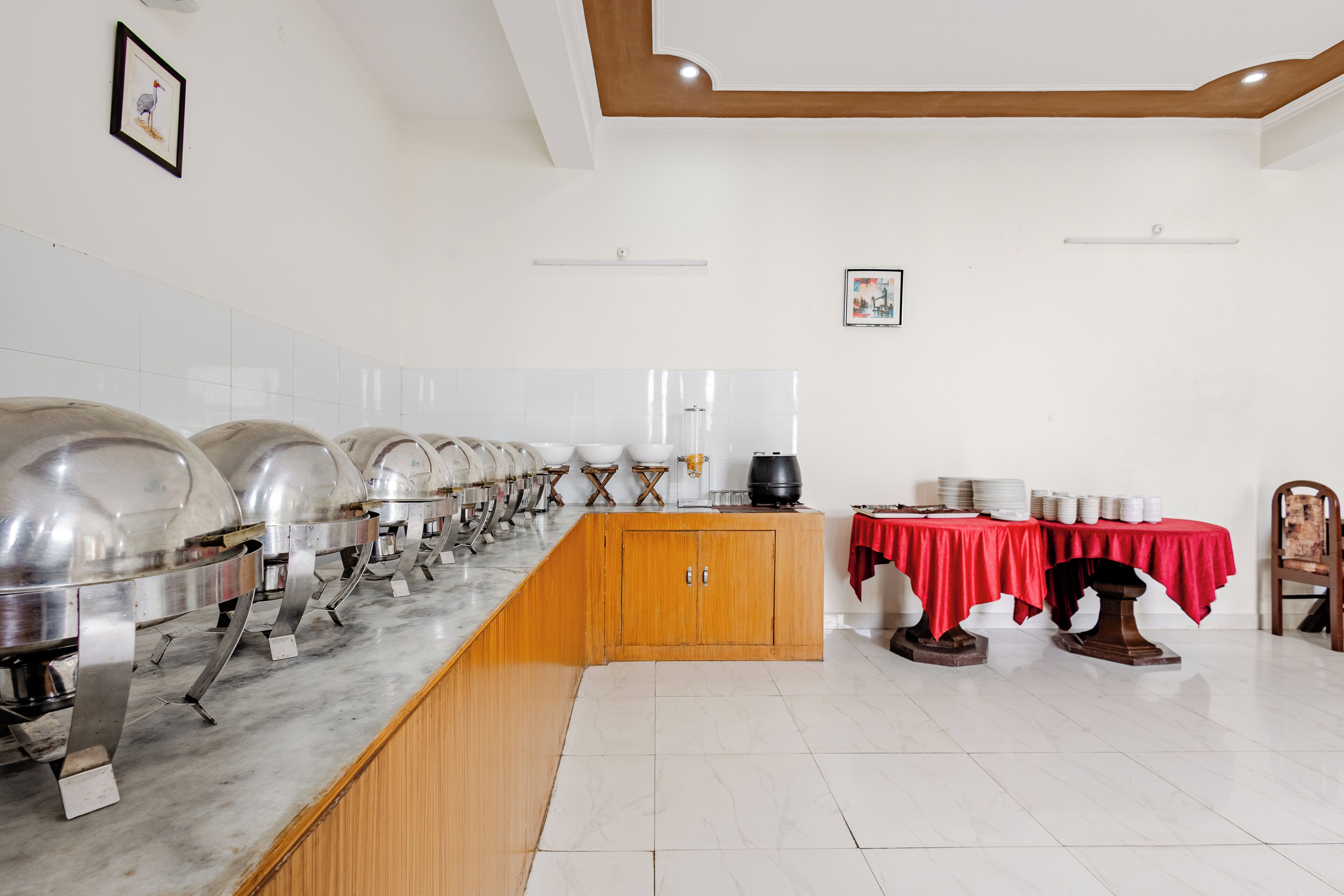 A buffet setup with multiple food stations, a wooden cabinet, and a table with a red tablecloth.