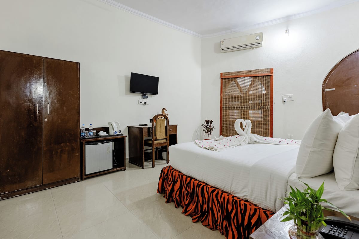 Une chambre d’hôtel comprenant un lit, un bureau, une télévision, une armoire et une fenêtre avec un store en tissu.