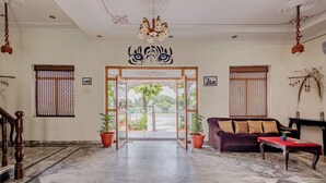 Um hall espaçoso com piso de mármore, escada de madeira, um sofá e uma mesa vermelha.