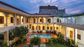 Um pátio com piscina, rodeado por edifícios com arcadas e telhado em azulejos.