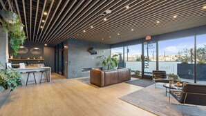 A modern interior with a wooden ceiling, a seating area with a sofa and chairs, a kitchen counter, and a large window offering a city view. - The Speakeasy- Walk to Broadway! Pool, Gym, Parking & More, Amazing Location (Nashville)