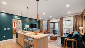 A modern living room with a large sofa, a coffee table, and a kitchen area with a central island. - The Speakeasy- Walk to Broadway! Pool, Gym, Parking & More, Amazing Location (Nashville)