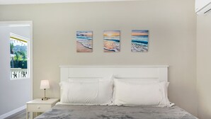A bedroom with a bed, white headboard, and three paintings of the ocean on the wall.