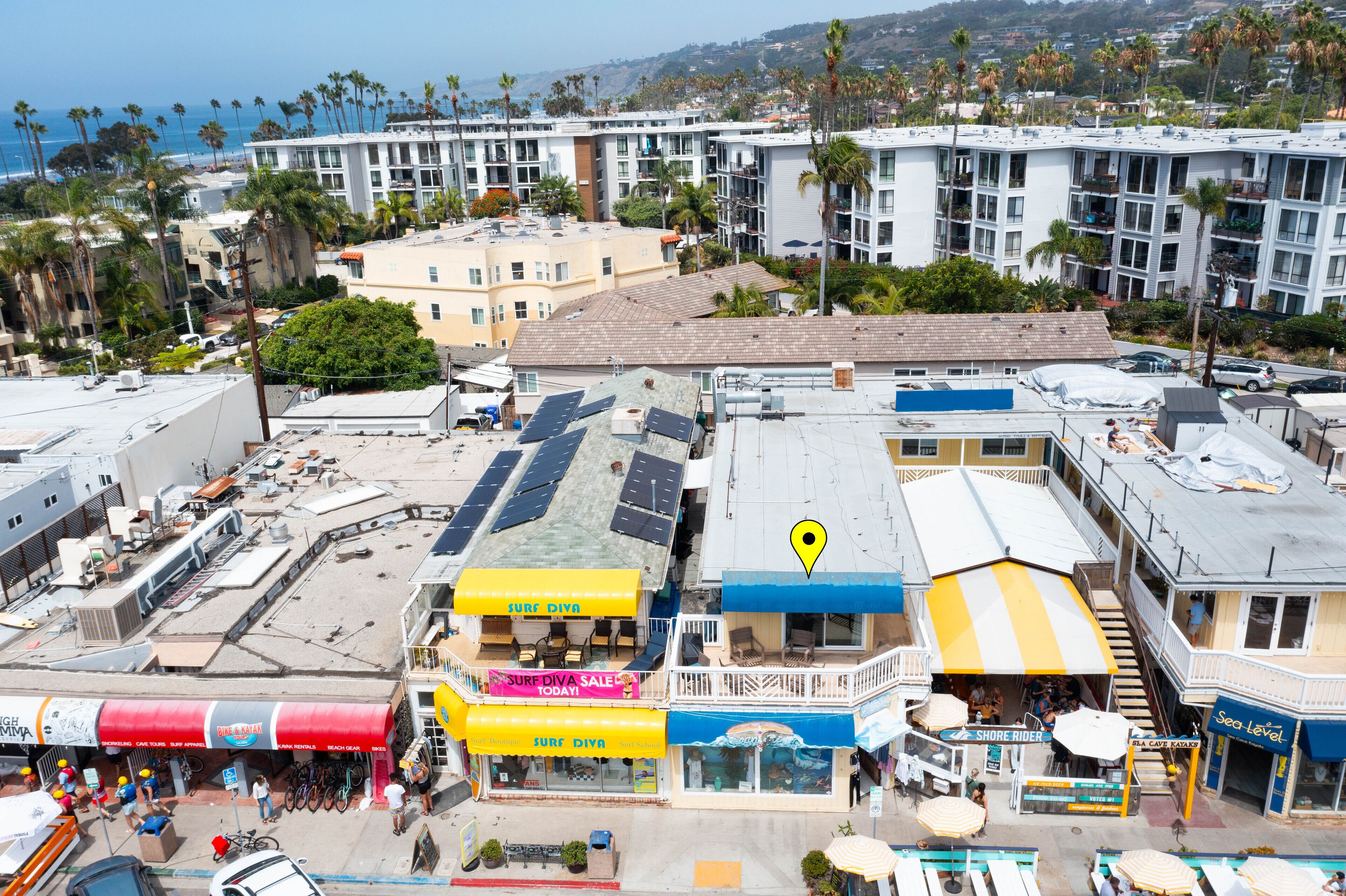Un immeuble à plusieurs étages doté d’un ensemble de panneaux solaires sur le toit, d’un magasin de surf et d’un restaurant avec une terrasse.