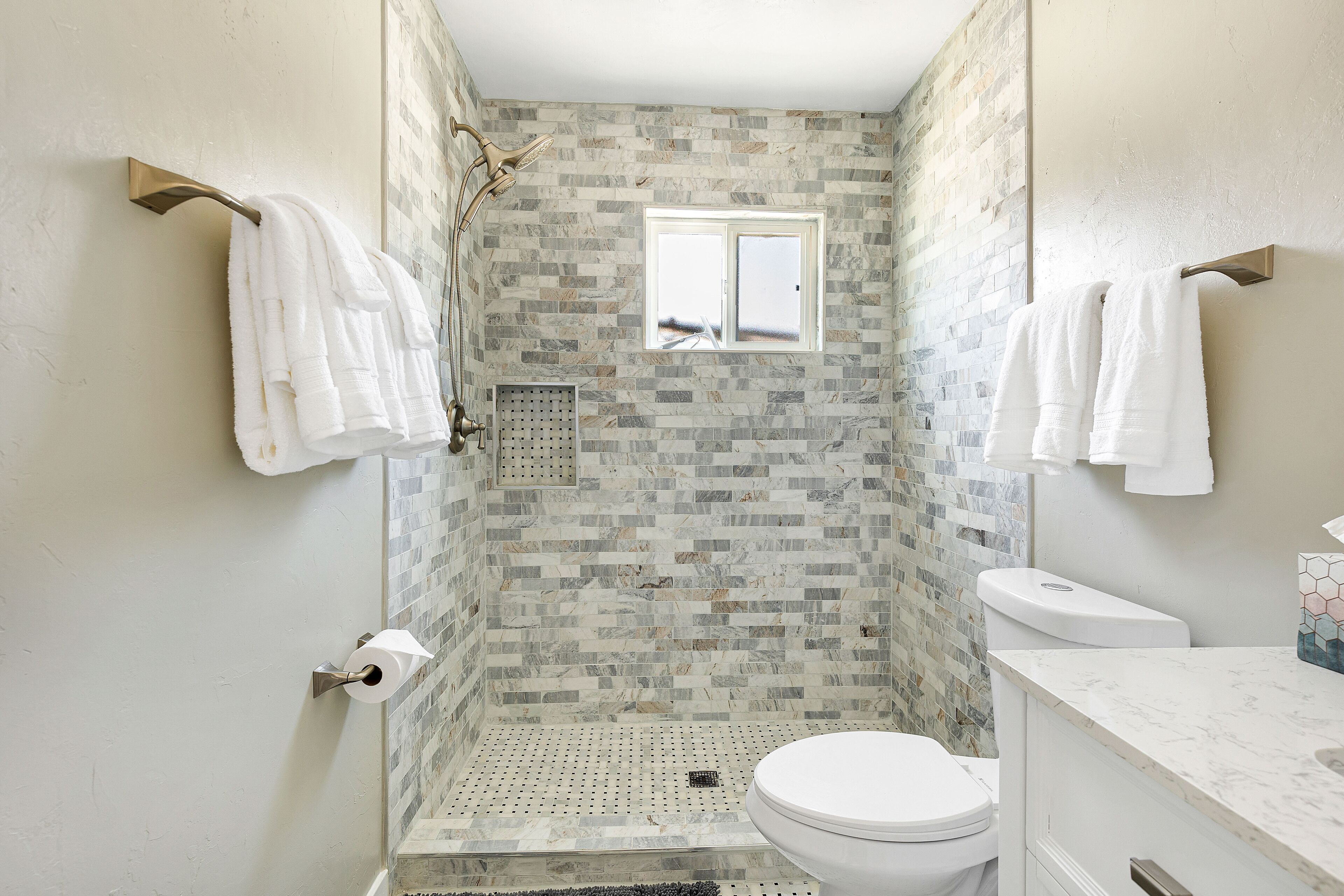 A bathroom with a shower, toilet, and sink, featuring a mosaic tile wall and a window.