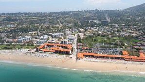 An aerial view of a coastal city with a beach, buildings, and a hilly background.