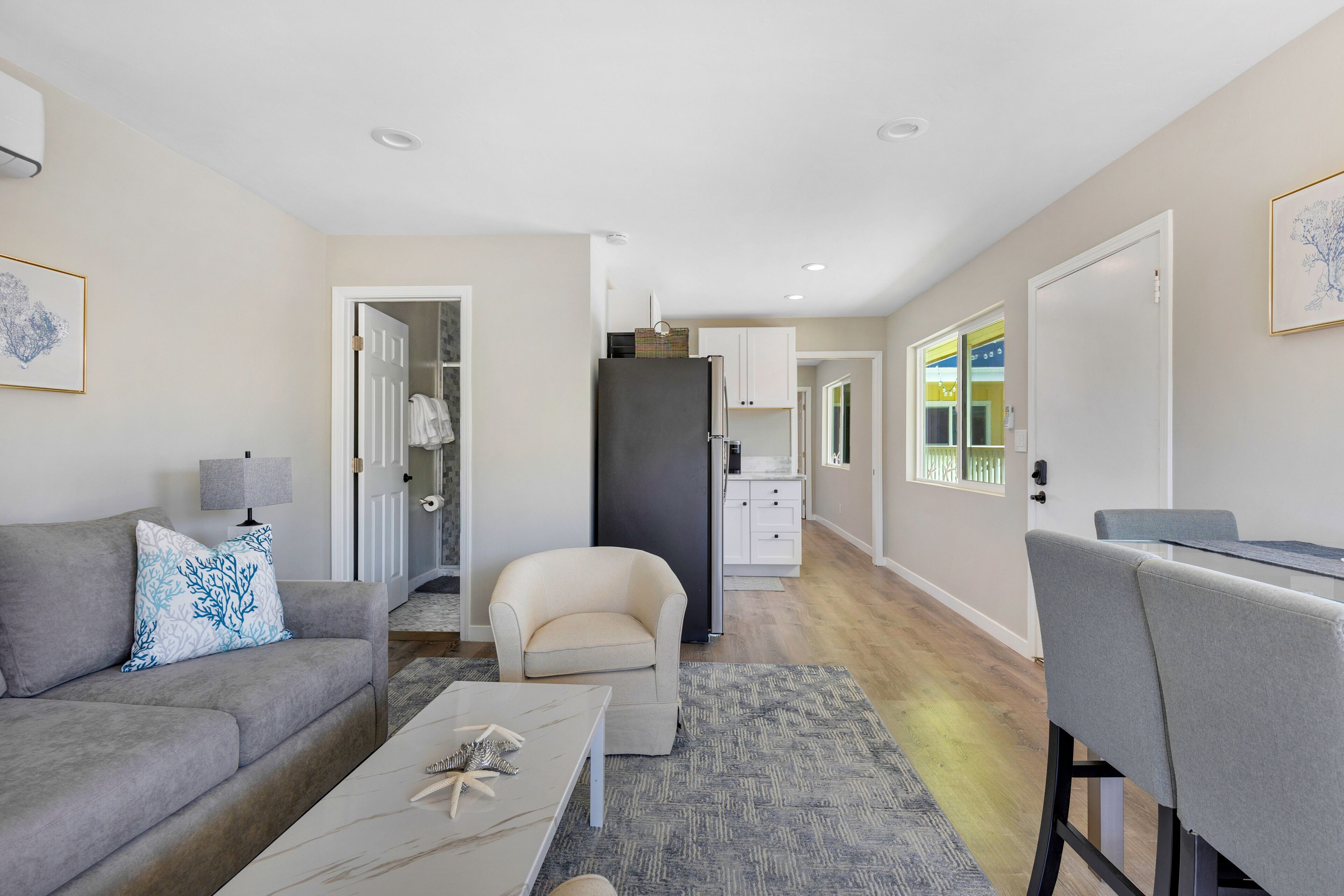 A modern living room with a grey sofa, a coffee table, and a dining area with a grey chair.