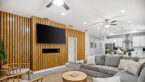 Una sala de estar moderna con una pared de acento de madera, un televisor de pantalla plana, un sofá seccional gris y una mesa de centro redonda.