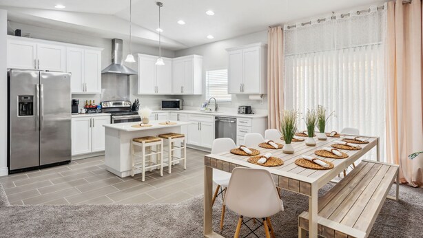 Una cocina moderna con armarios blancos, electrodomésticos de acero inoxidable y un comedor con mesa y sillas de madera.