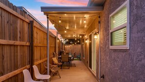 Un patio cubierto con cerco de madera, mobiliario exterior, luces colgantes y vistas al cielo.