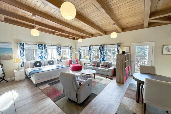 A spacious room with a bed, two sofas, a red armchair, a dining table, and a large window with curtains.