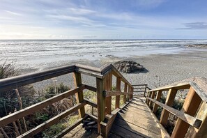 A wooden boardwalk leading to a beach with pebbles and a rocky outcrop.