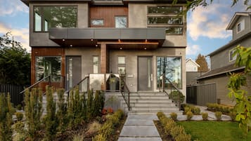 A modern two-story house with a concrete exterior, large windows, and a visible staircase leading to the entrance.
