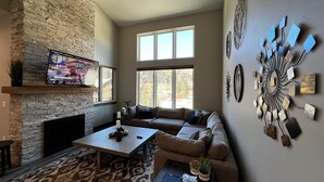 A living room with a stone fireplace, a large window, a sofa, a coffee table, and wall art. - Beautiful 3-bedroom townhome at Purgatory Resort with mountain views, perfect for families. (Durango)