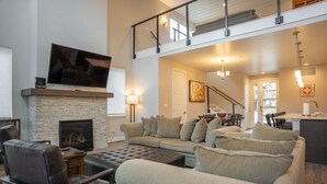 A modern living room with a fireplace, a television, and a dining area with a staircase.