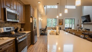 A modern kitchen with stainless steel appliances, a large island with a sink, and a dining area with a TV.