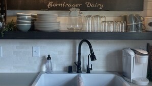 A kitchen with a farmhouse aesthetic, featuring a wooden sign that reads "FARM FRESH MILK," a sink with a modern faucet, and a coffee maker.