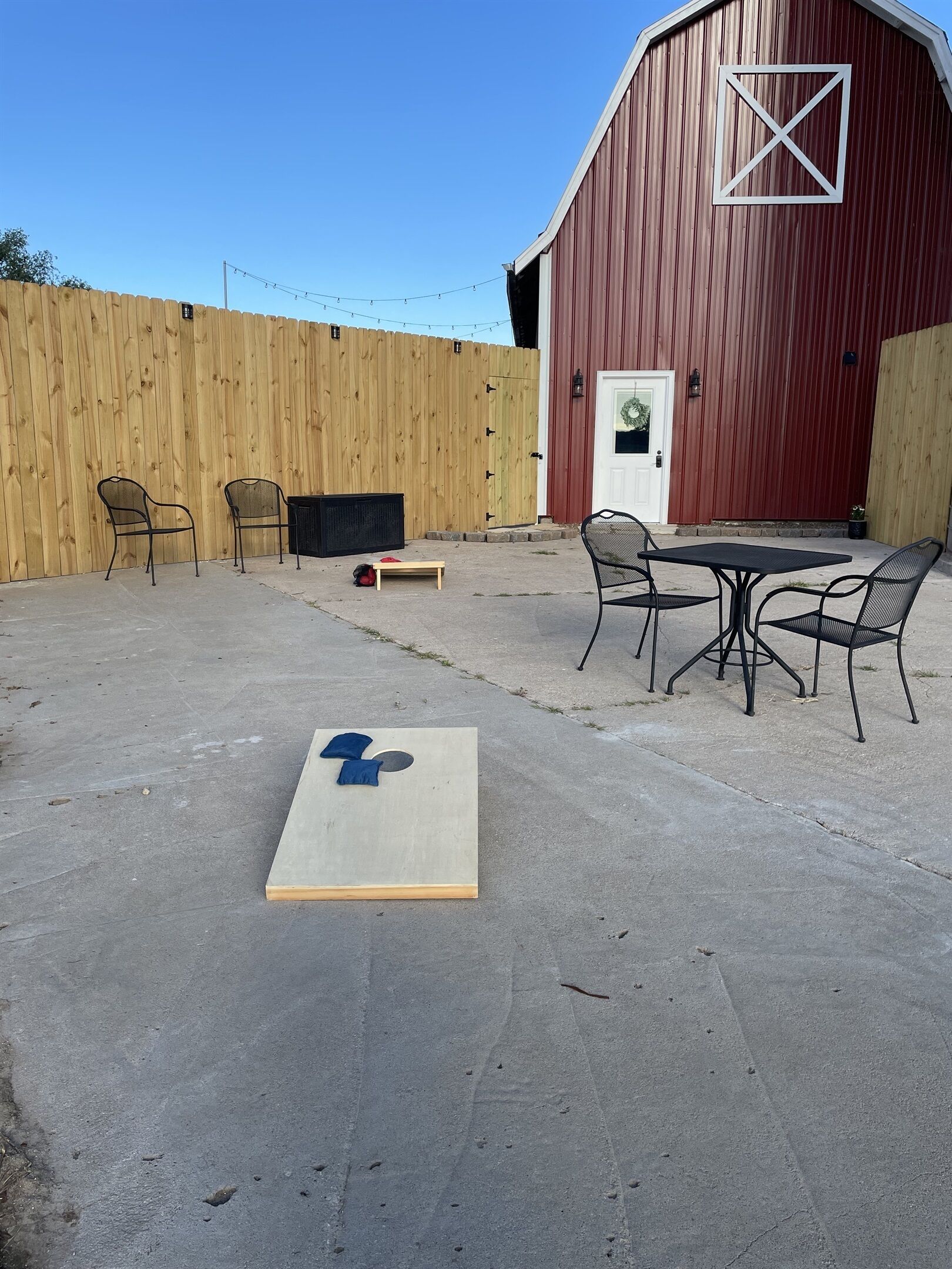 Een terras buiten met een betonnen vloer, een houten omheining en een rode schuur op de achtergrond.