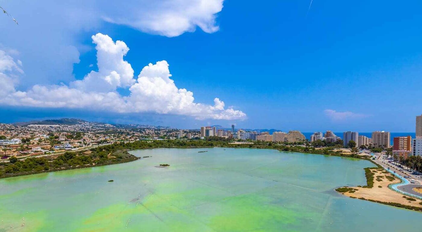 A coastal cityscape with a large body of water, urban buildings, and a clear sky.