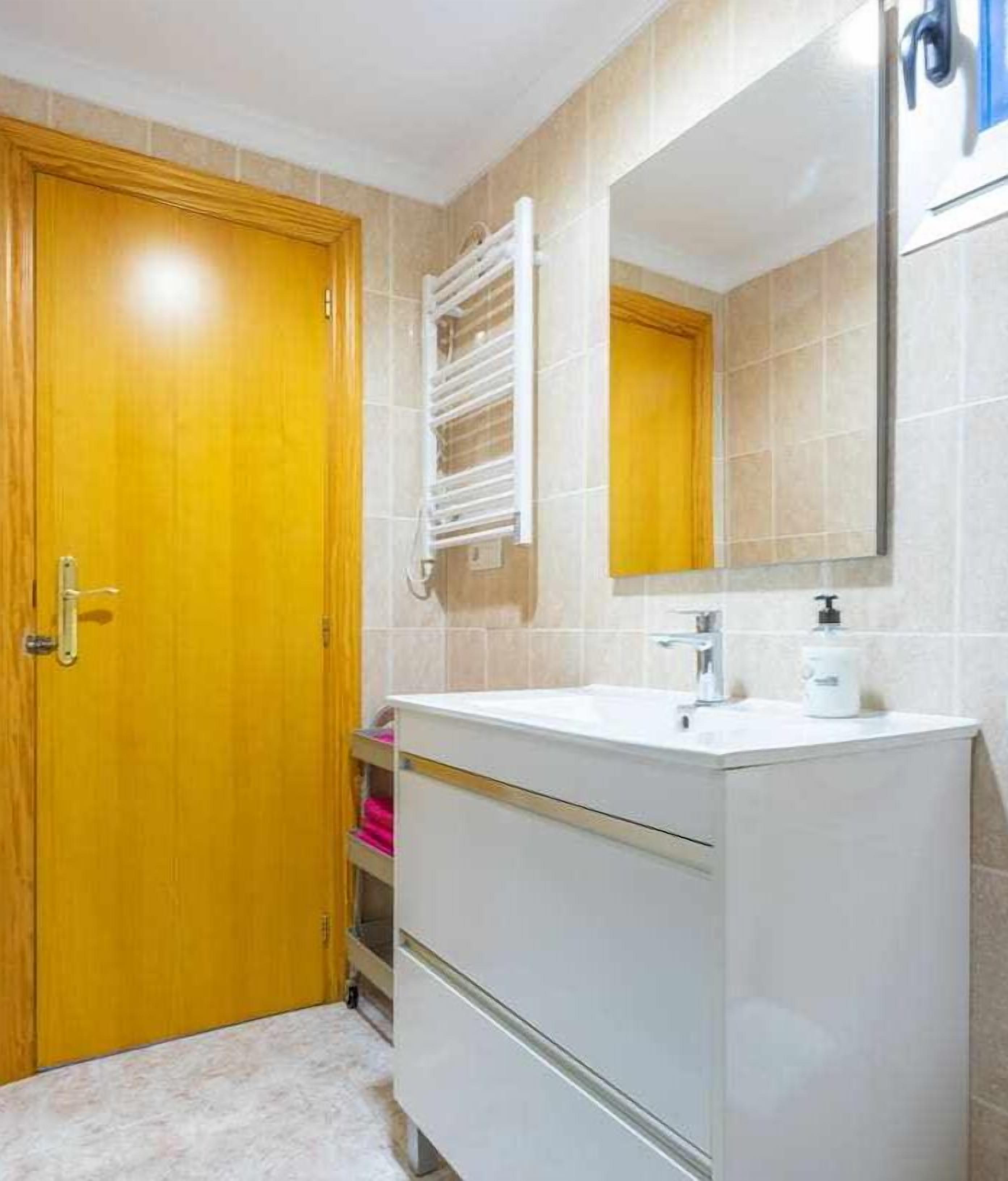 A bathroom with a wooden door, a white sink with a mirror above it, and a towel rack.