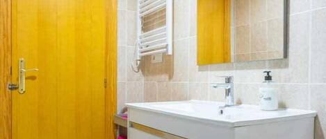 A bathroom with a wooden door, a white sink with a mirror above it, and a towel rack.