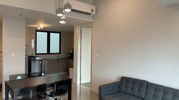 Una sala de estar moderna con un sofá gris, una mesa de comedor de vidrio con sillas y una cocina con ventana y electrodomésticos integrados.