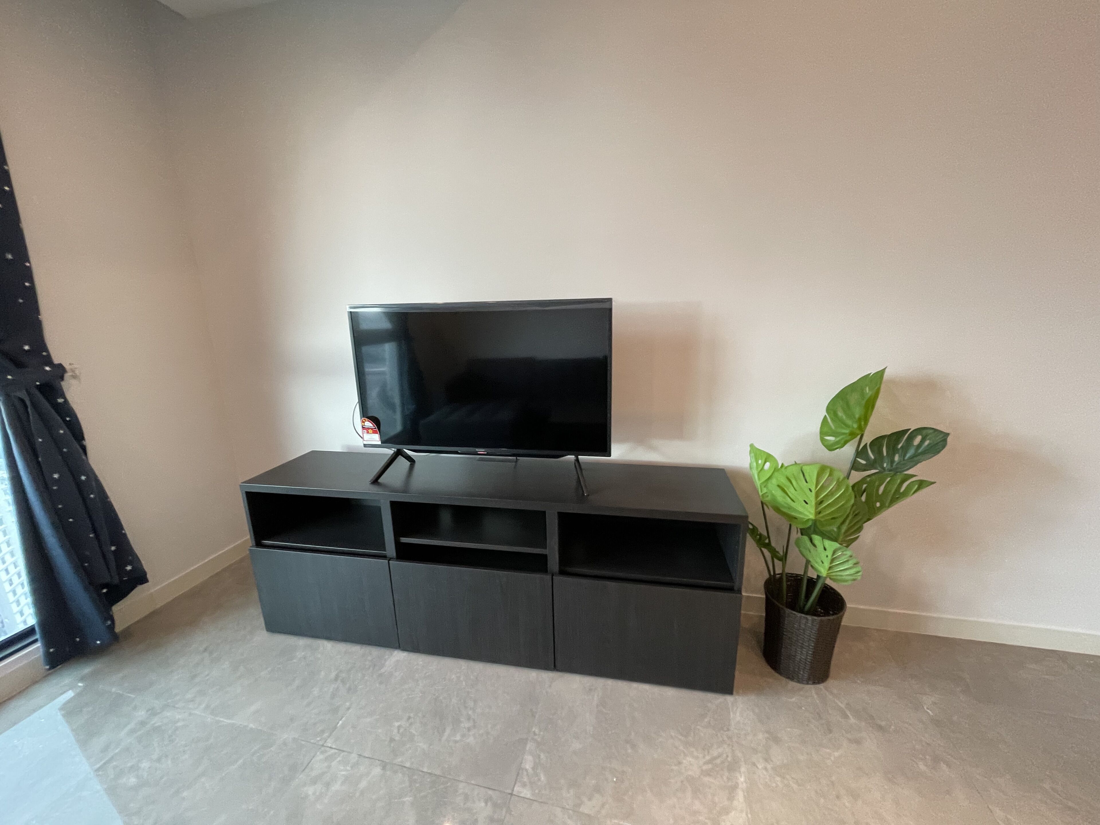 A black entertainment unit with a flat-screen TV, a potted plant, and a window with curtains.
