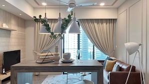 Un salon moderne avec une table à manger en bois, deux chaises blanches, un canapé en cuir marron, un téléviseur et un ventilateur de plafond.