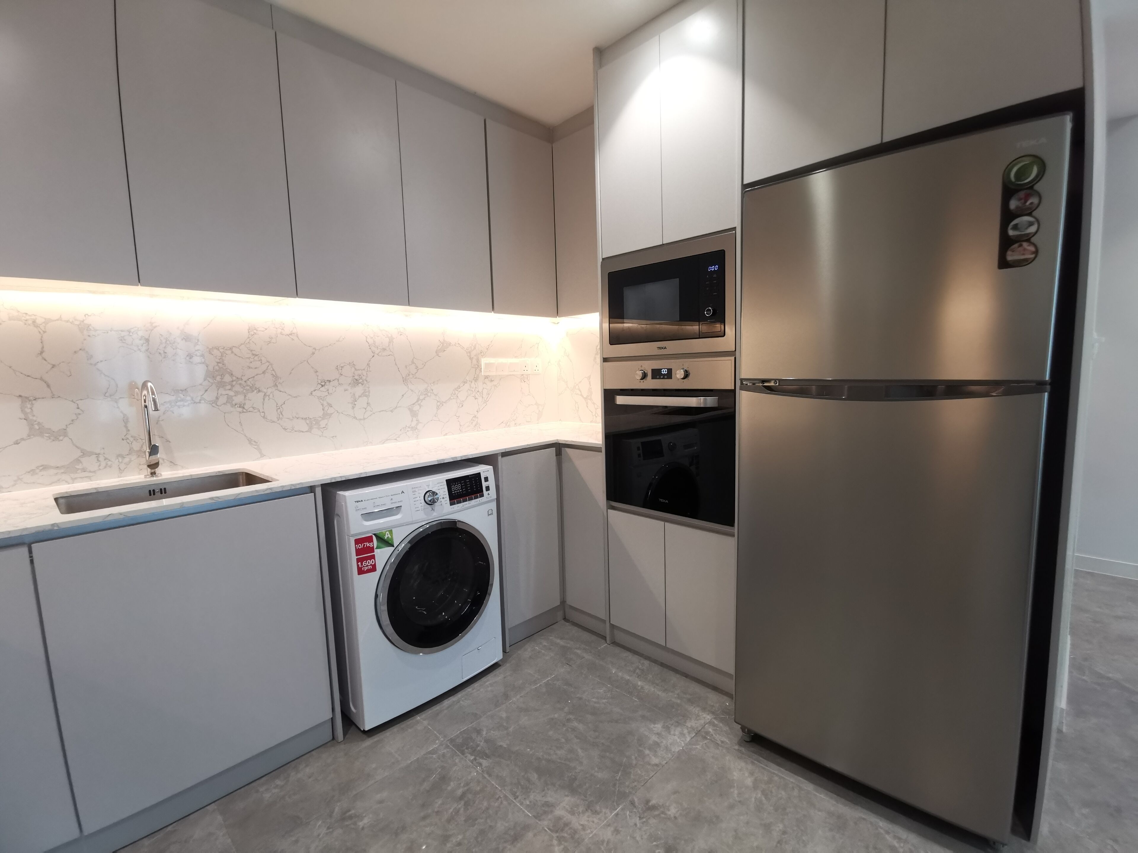 A modern kitchen with built-in appliances including a stainless steel refrigerator, microwave, oven, and a front-loading washing machine.