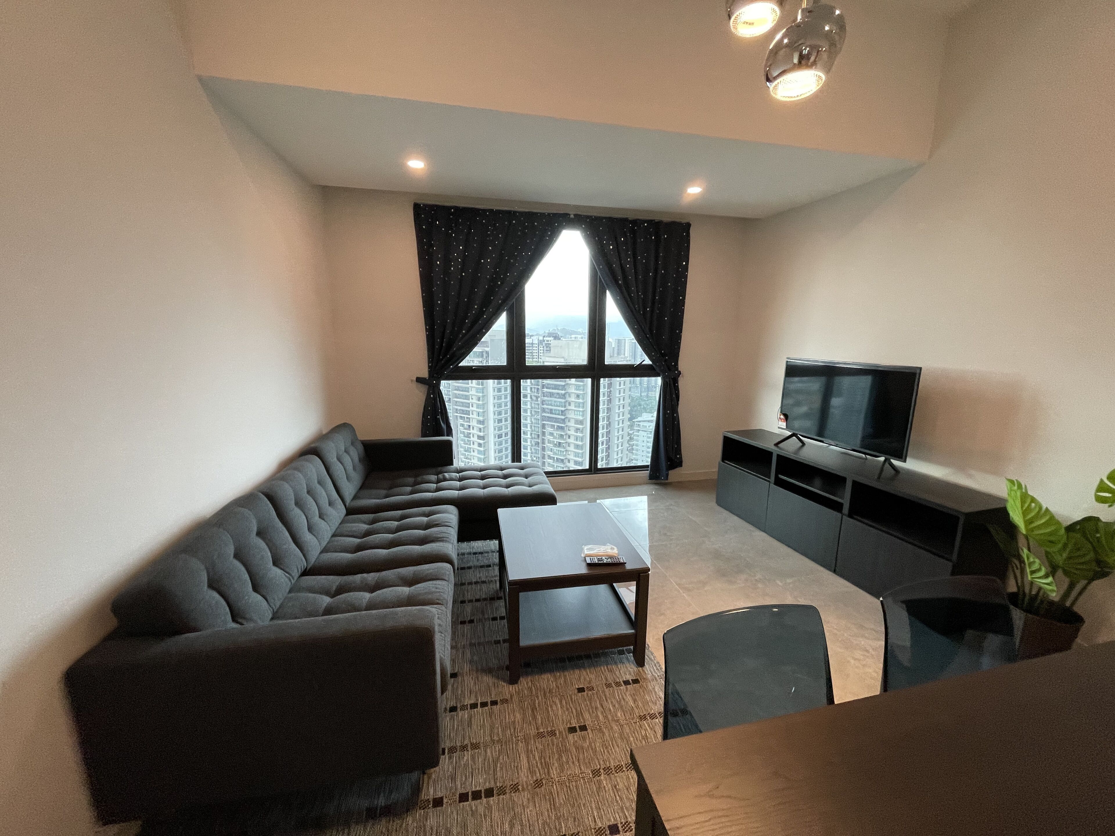 A modern living room with a sectional sofa, a coffee table, a flat-screen TV, and a large window with curtains.