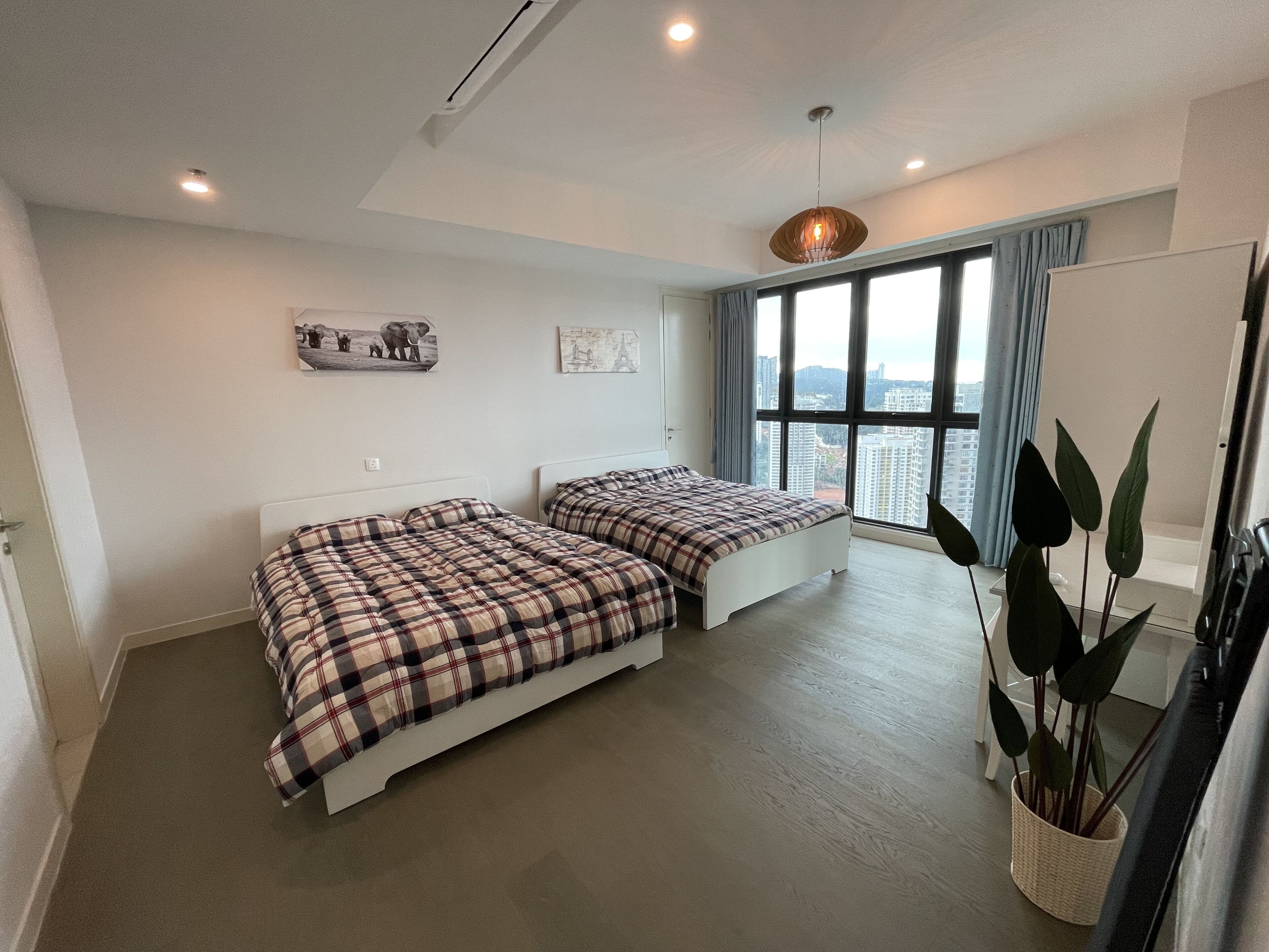 Une chambre moderne avec deux lits, de grandes fenêtres, une vue sur la ville et un luminaire suspendu.
