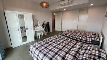 A bedroom with two beds, a white wardrobe, a dressing table with a mirror, and a hanging light fixture.