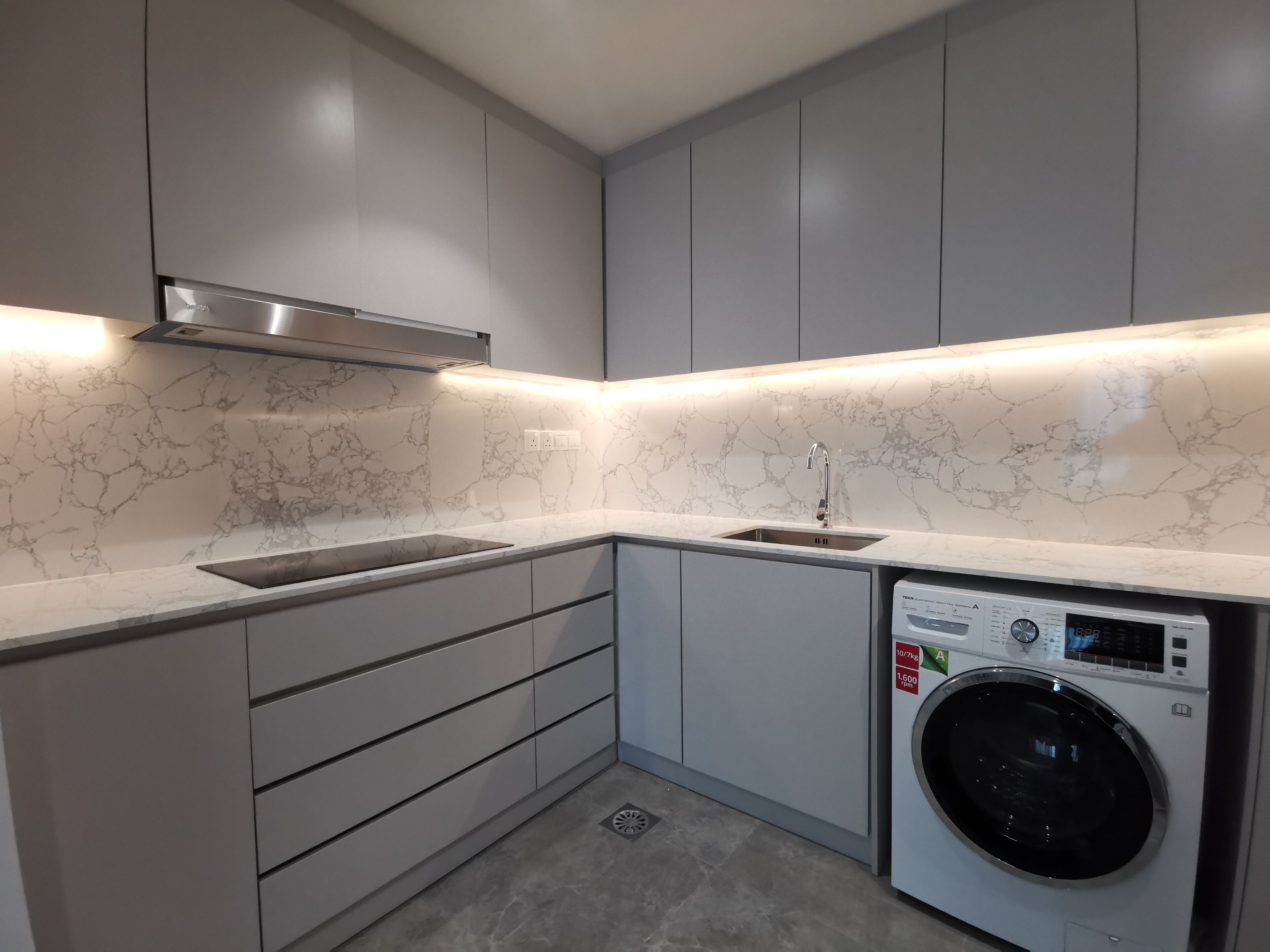 A modern kitchen with grey cabinets, a built-in sink, and a front-loading washing machine.
