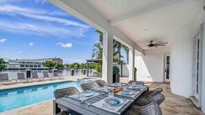 A covered outdoor dining area with a pool view, wicker furniture, and a ceiling fan.